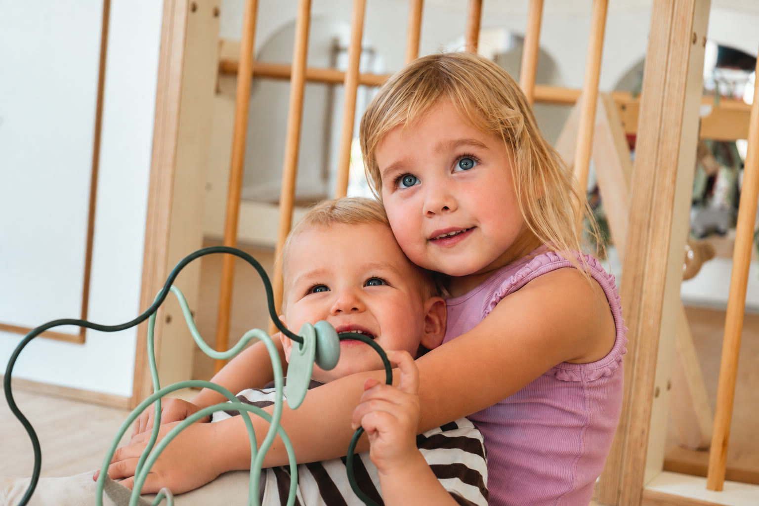 Twee kinderen die binnen op de vloer spelen met een houten kralenspiraal